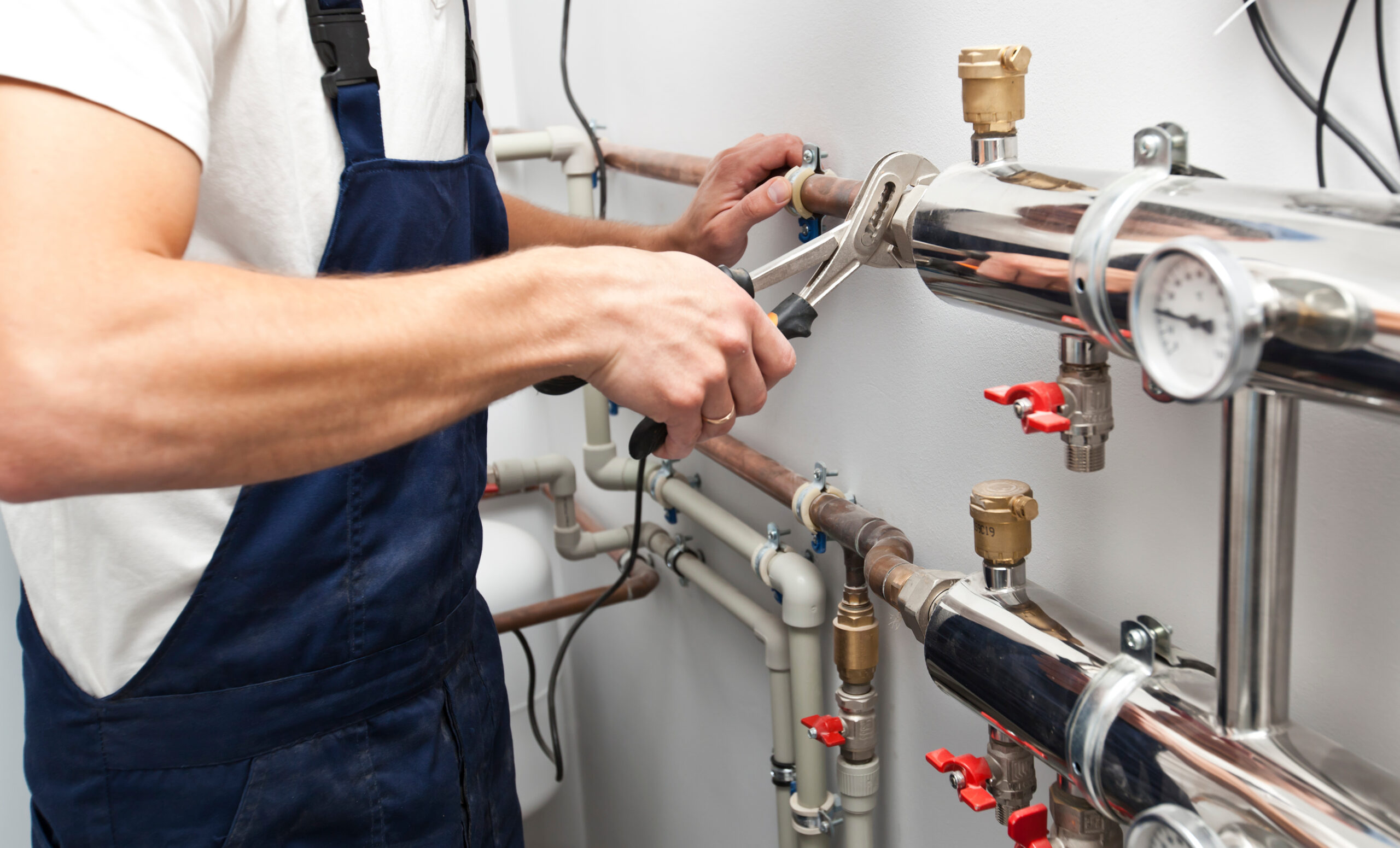 The man is installing the heater system in the house and checking pipes by the wrench